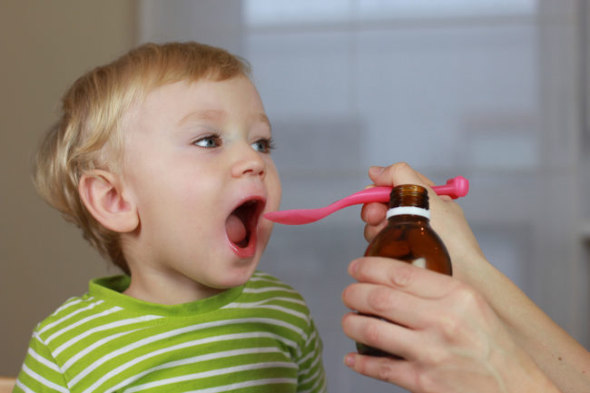 Мальчик пьет лекарство из ложечки с широко открытым ртом