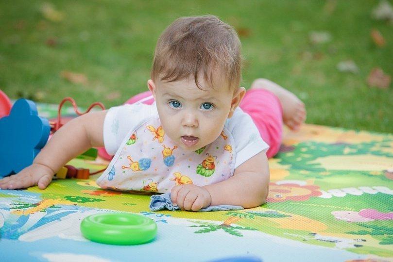 Ребенок 9 месяцев лежит на коврике на животике и играется игрушками