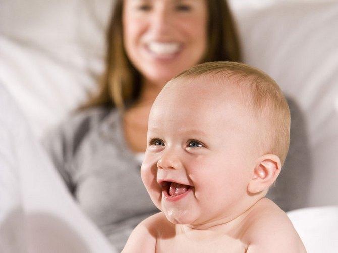Ребенок 9 месяцев сидит рядом с мамой и улыбается