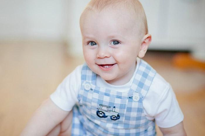 Ребенок в белой футболке и голубом полосатом комбинезоне сидит на полу