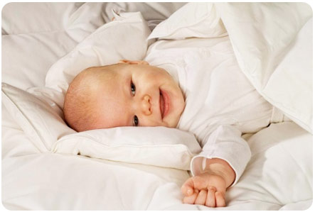 Ребенок лежит в кроватке под одеялом и улыбается