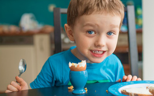 Мальчик в синей футболке ест яйцо всмятку