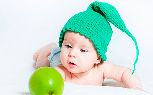 Ребенок в зеленой вязаной шапочке смотрит на яблоко