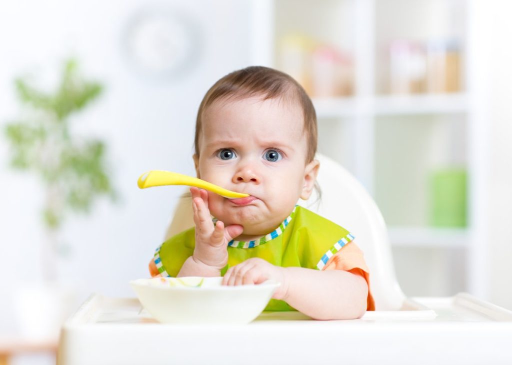 Ребенок ест ложку и сидит за столом